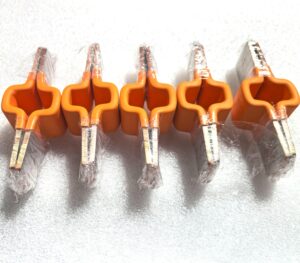 Overmolded copper busbar connector featuring stacked copper conductors, flat metallic contact ends, and an orange insulating body. Designed for electrical connections in battery assemblies, with custom configurations for OEM integration.